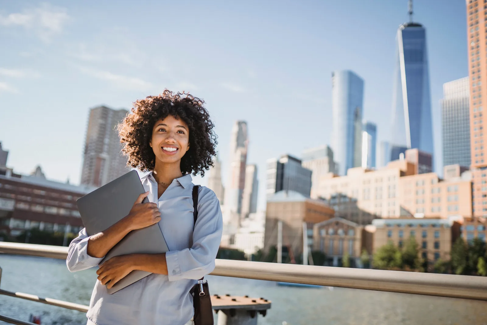 Smiling woman with laptop in a cityscape, embodying urban professionalism. Where demand for a virtual assistant agency is strongest