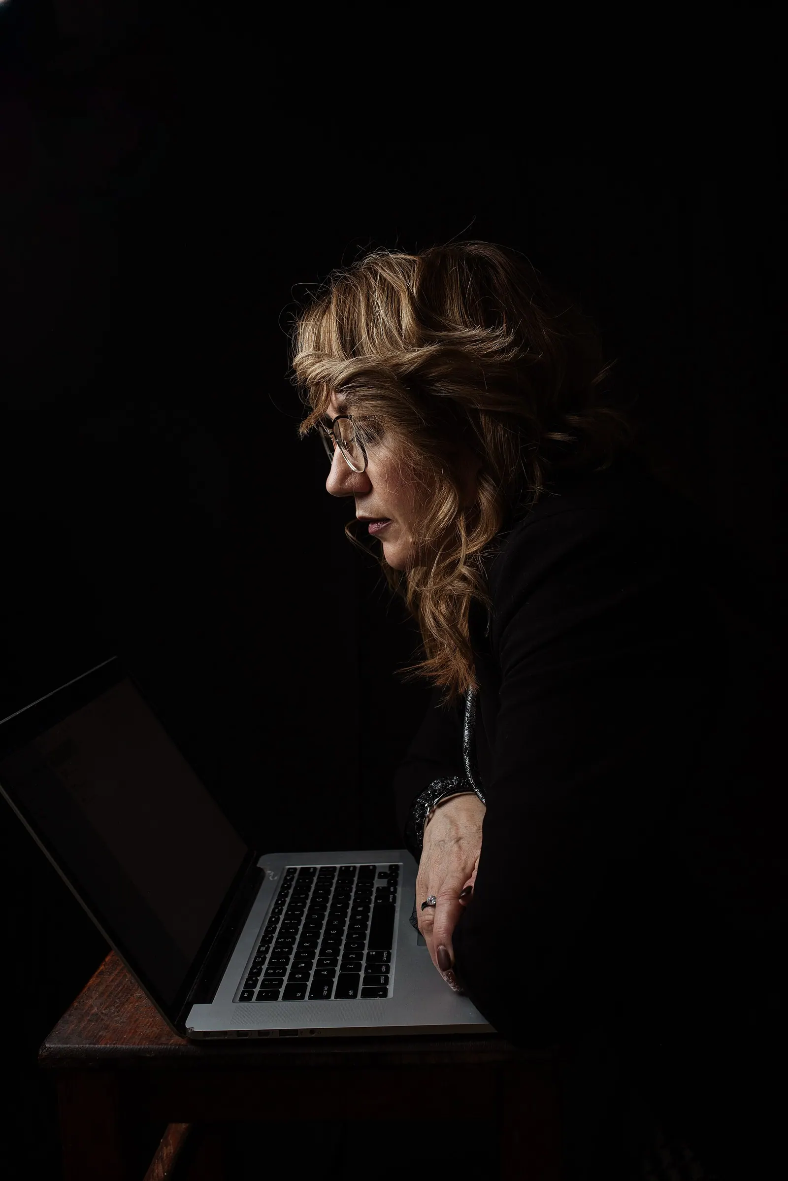 A focused middle aged woman uses a laptop while working late at night in a low-light apartment interior. The image illustrates remote work, concentration, digital communication and. CRA contractor rules for a virtual assistant agency: the factors that decide