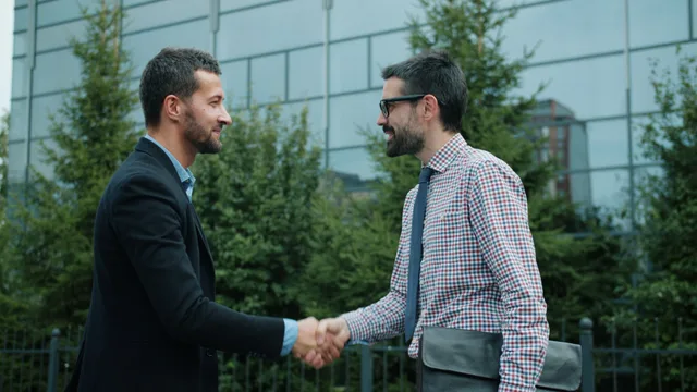 Two men shaking hands outside a modern office building, symbolizing business partnership. Virtual assistant agency contracts: the six clause groups that prevent disputes