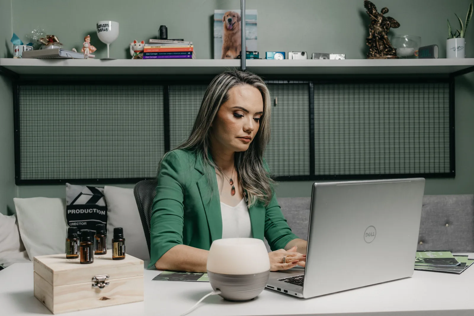 Woman in green jacket working on a laptop in a home office environment with essential oils. Virtual assistant agency profit margin: four layers and break-even reserved hours