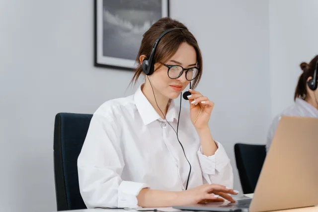 Young woman in glasses and headset providing customer support at a laptop in an office setting. Why virtual assistant agency clients quit within the first quarter